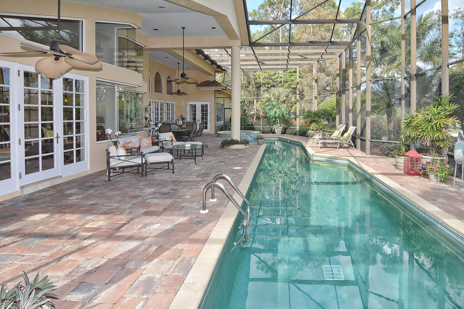 Covered patio with a long narrow pool, outdoor seating, and glass doors beside a leafy backyard