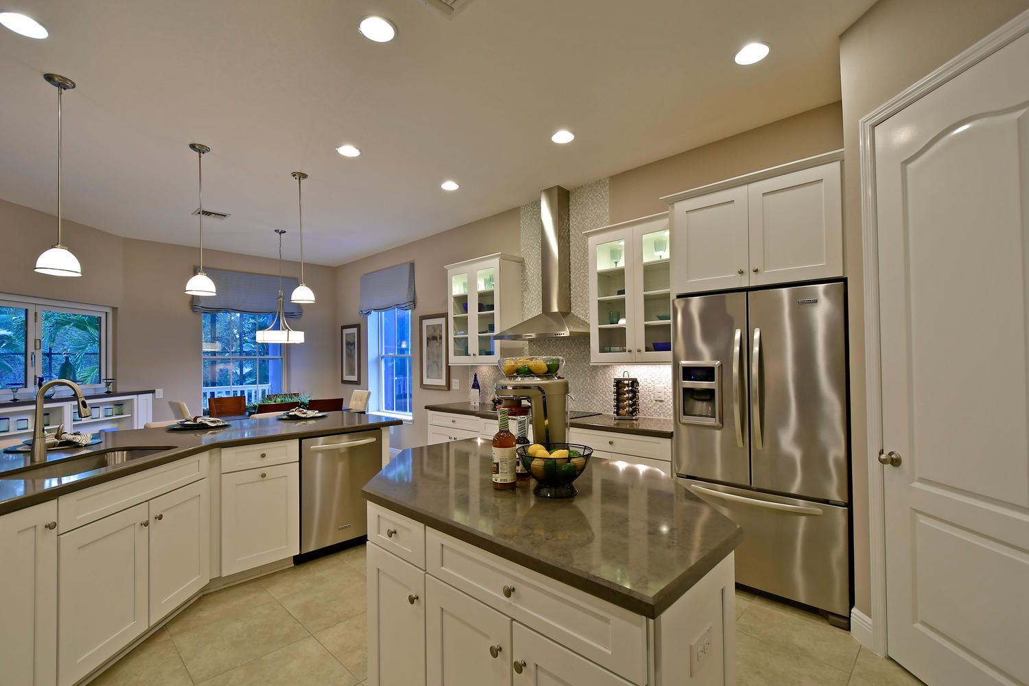 Bright modern kitchen with white cabinets, stainless steel appliances, and granite island under recessed lights