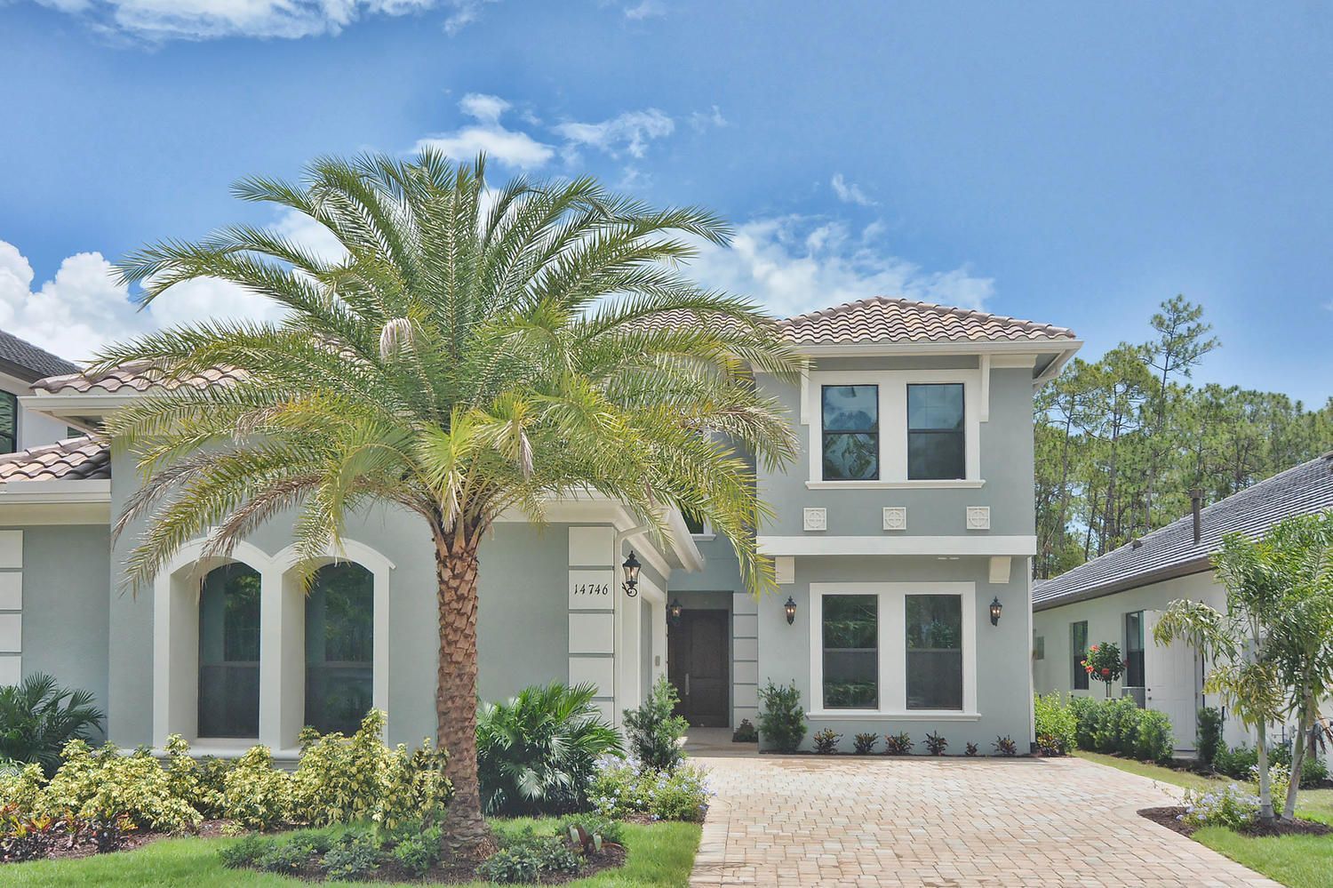 Two-story cream stucco house with a palm tree and tiled roof under a blue sky.