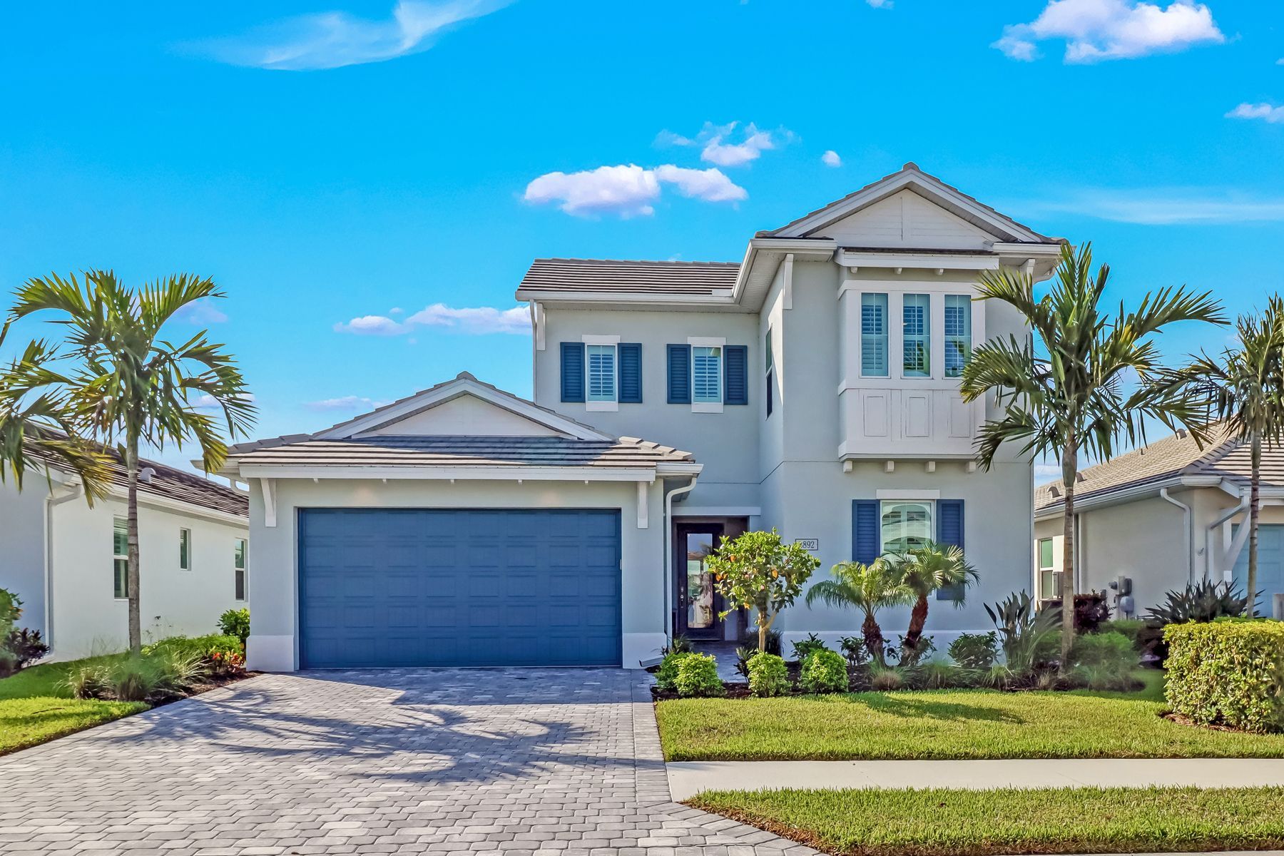 Two-story white house with blue garage door and shutters under a clear blue sky