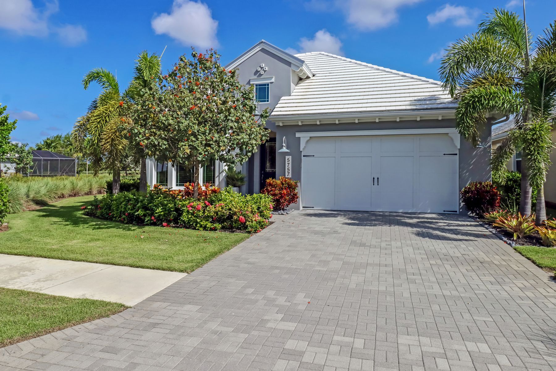 Suburban home with a gray garage, paver driveway, palm trees, and bright blue sky