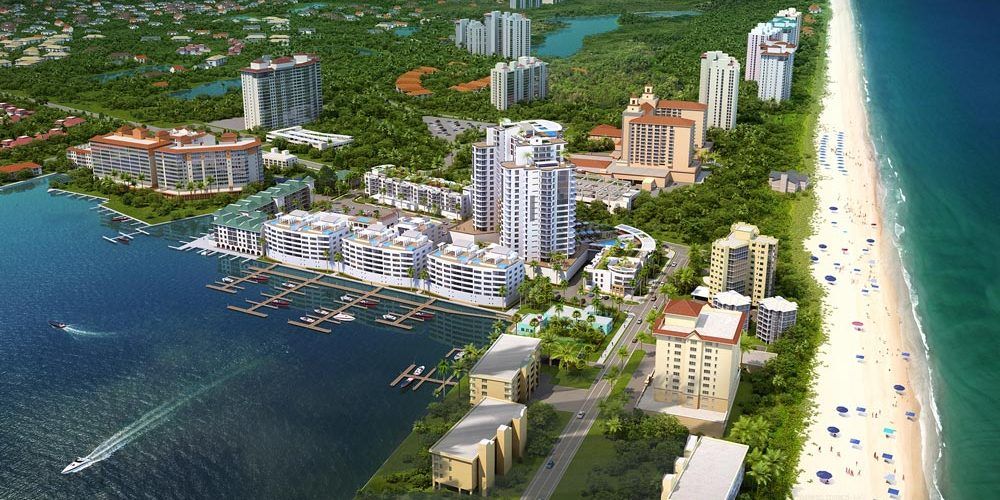 Aerial view of a beachfront resort with high-rise buildings, marina, blue water, and a sandy beach.