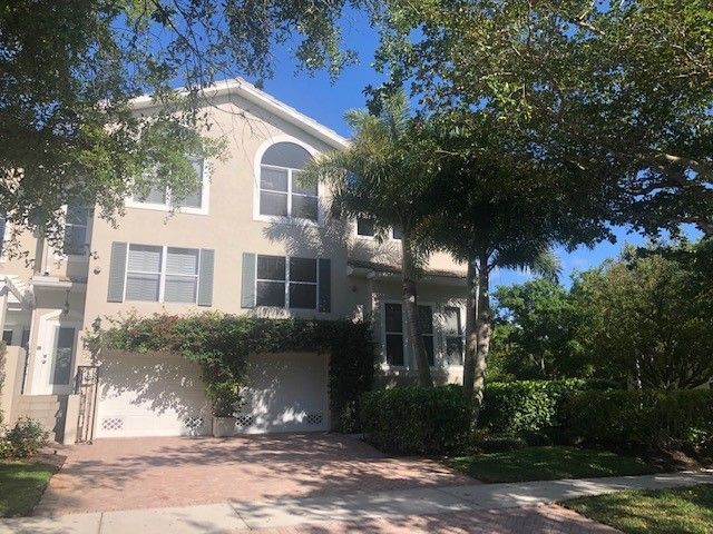 Two-story beige house with white trim, arched windows, a garage, and trees in front