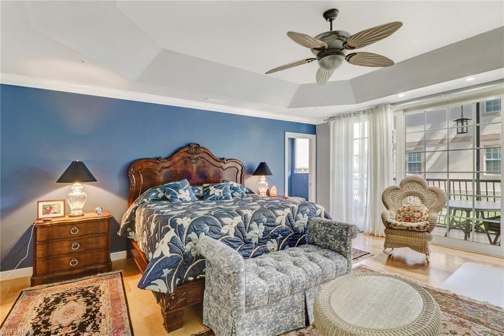 Bright bedroom with floral bedspread, blue accent wall, ceiling fan, and large window with balcony view