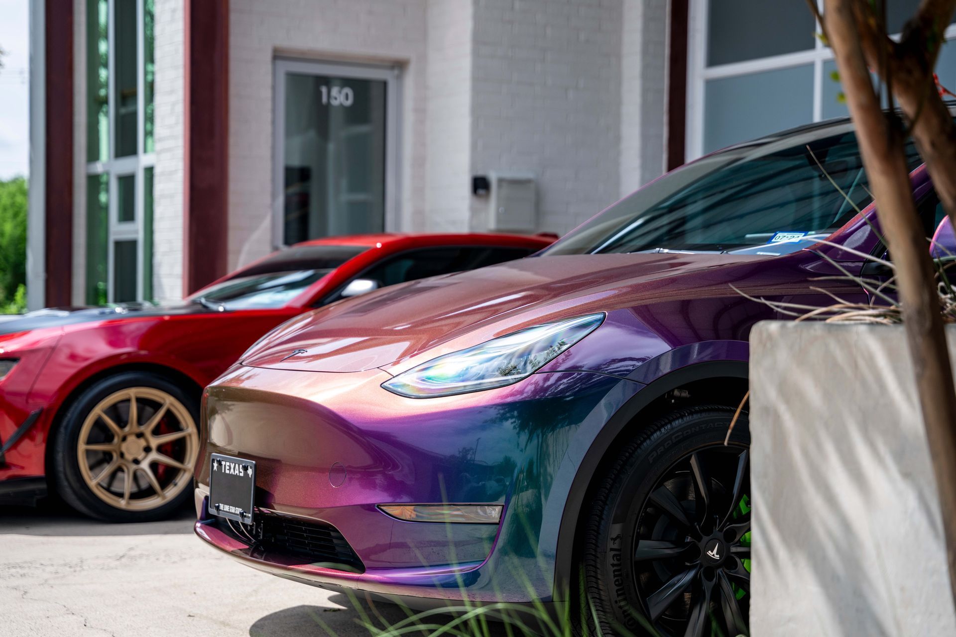 A colorful Tesla Model Y parked next to a red sports car in front of a building.