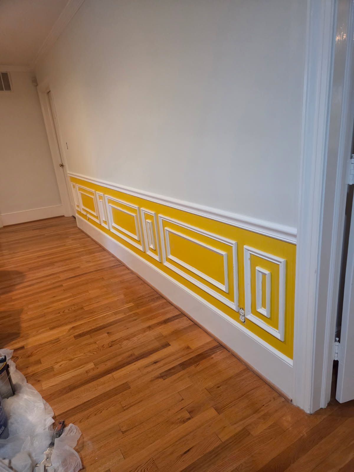 Yellow wainscoting with white trim along a wood-floored hallway, and white walls.