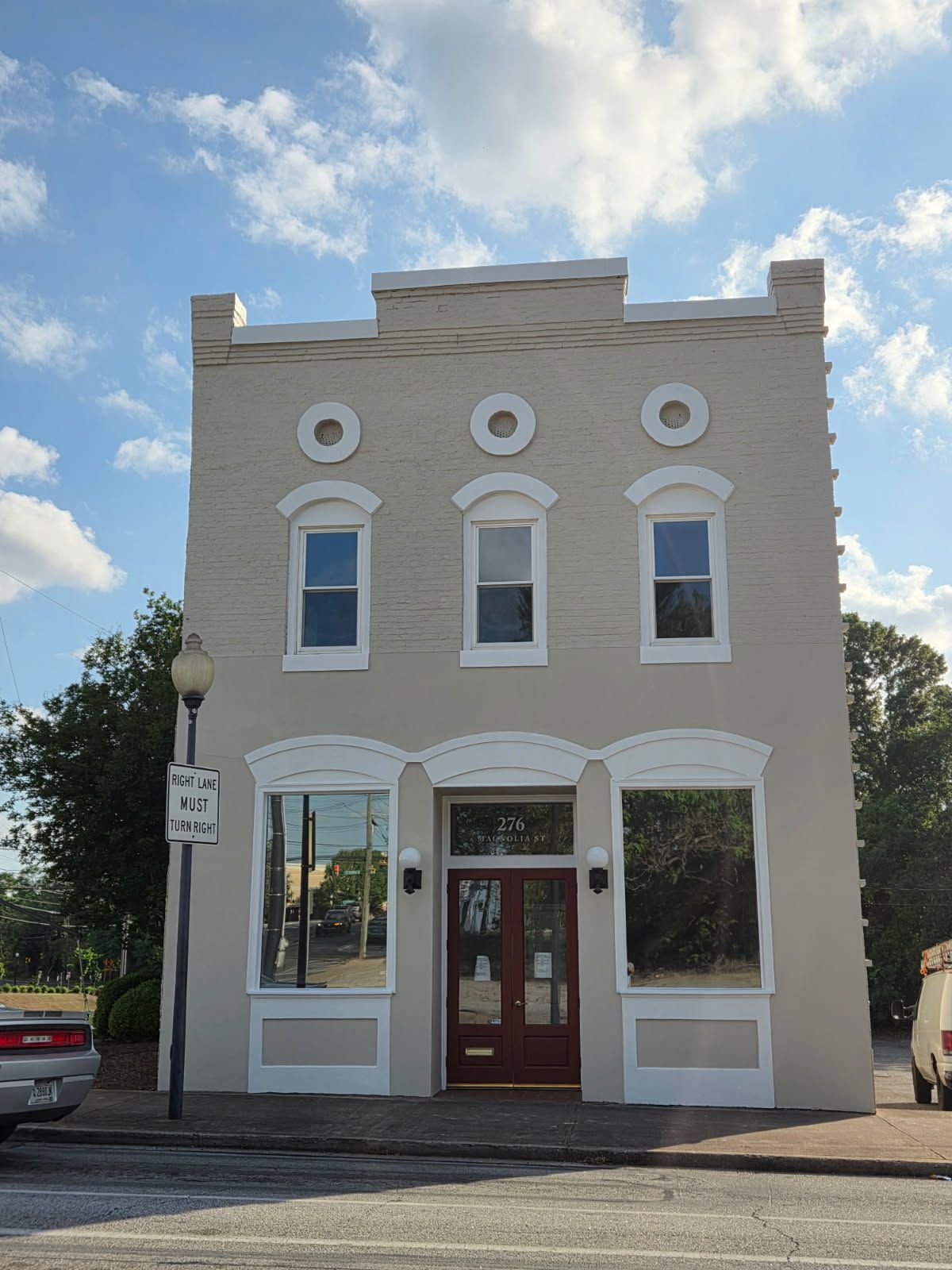 Two-story beige brick building with white trim around windows and decorative circles. Red door.