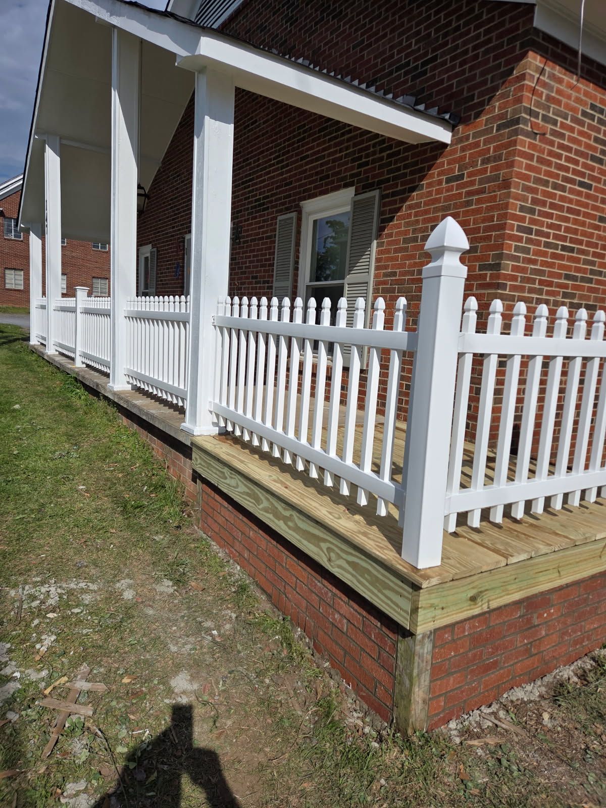 White picket fence around a porch of a brick building.