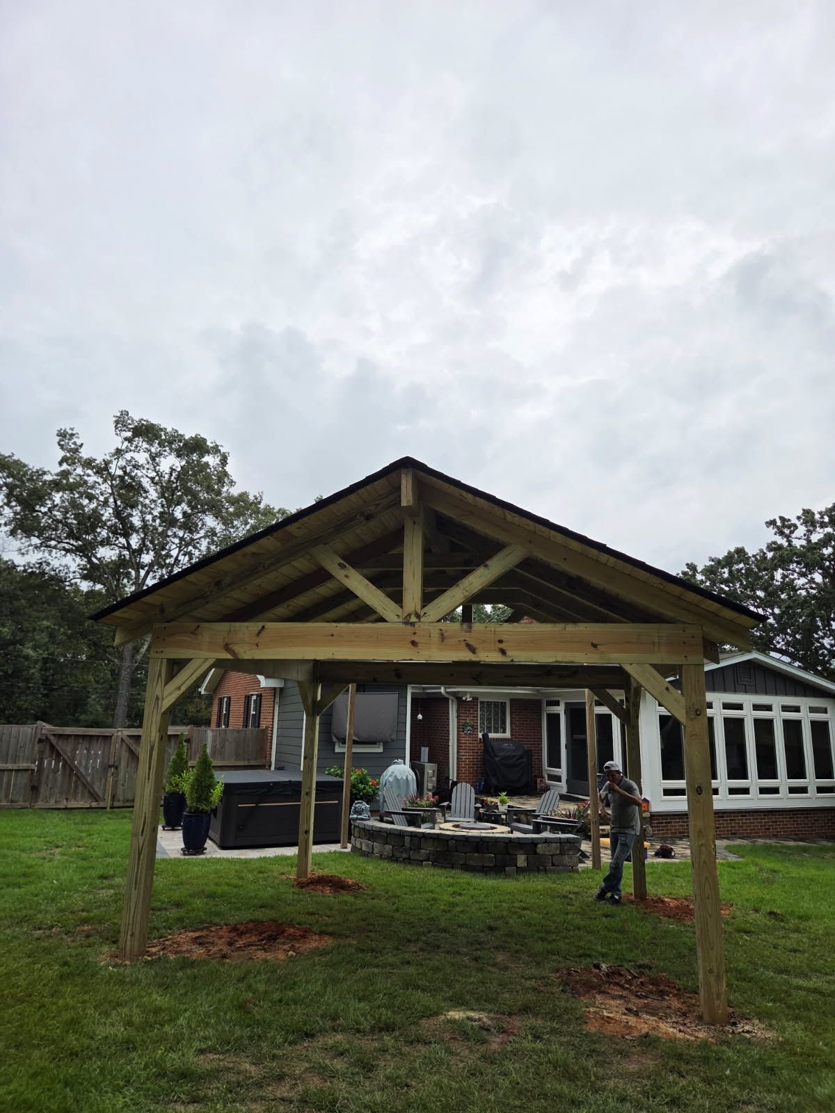 Wooden outdoor pavilion under construction in a grassy yard, with a partly cloudy sky.
