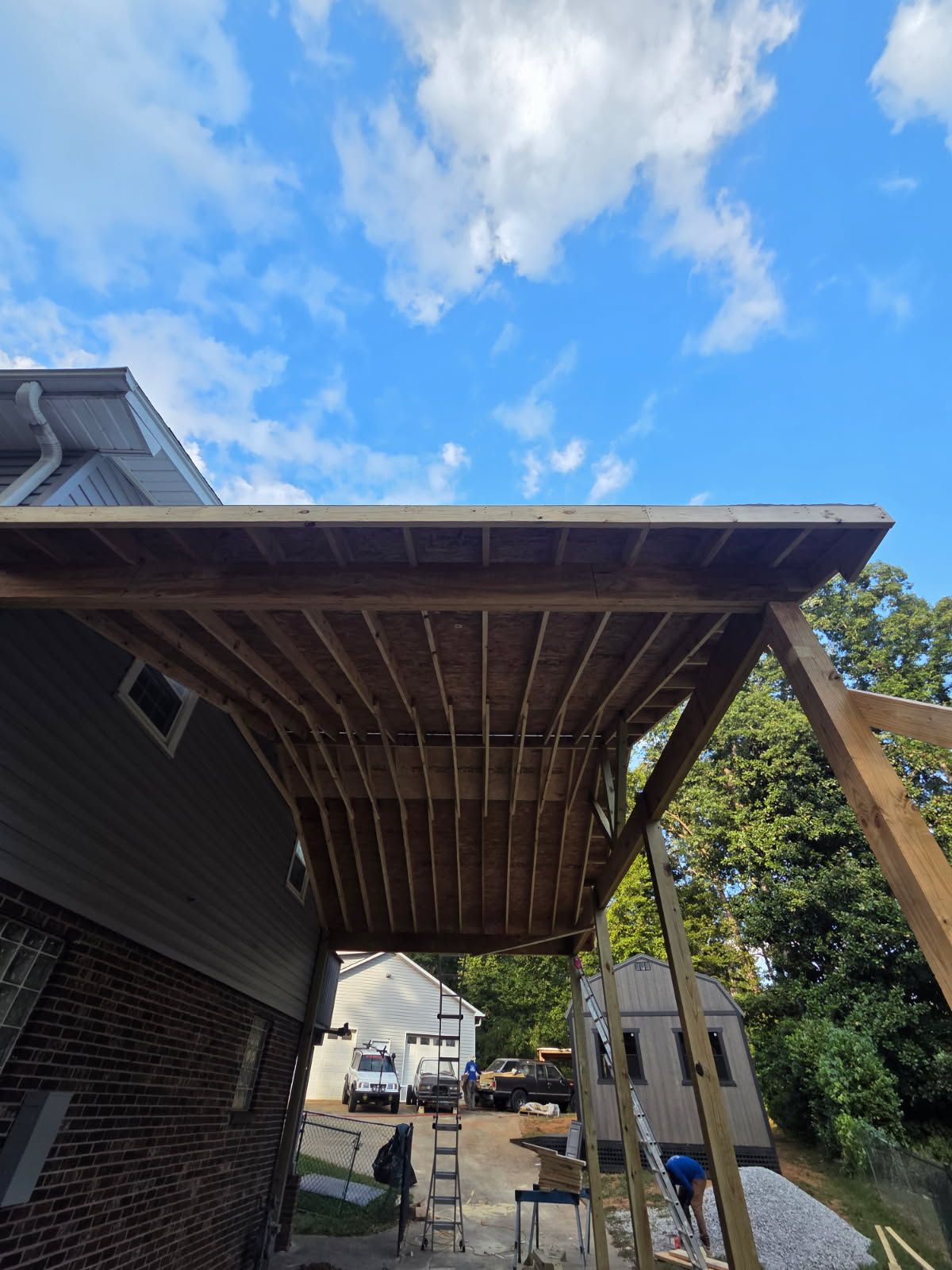 Construction of a wooden deck attached to a house; blue sky with clouds.