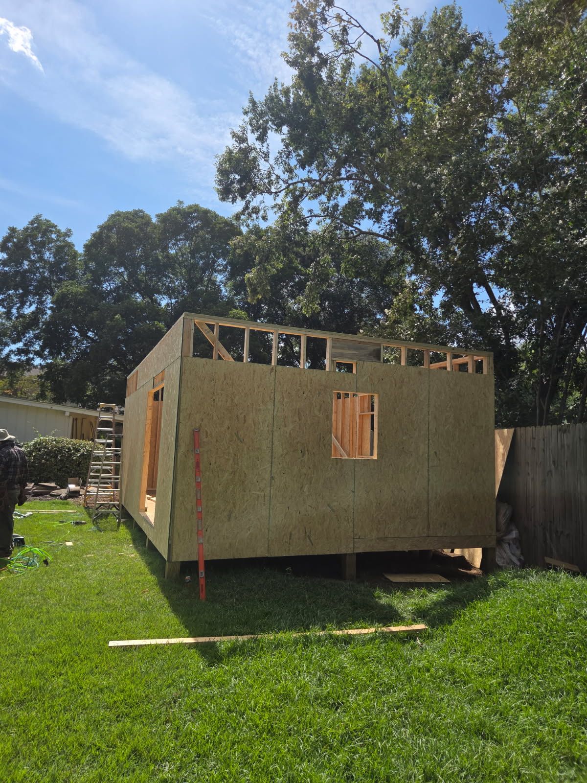 Wooden shed under construction in a grassy backyard, with a partially built roof and window frames.