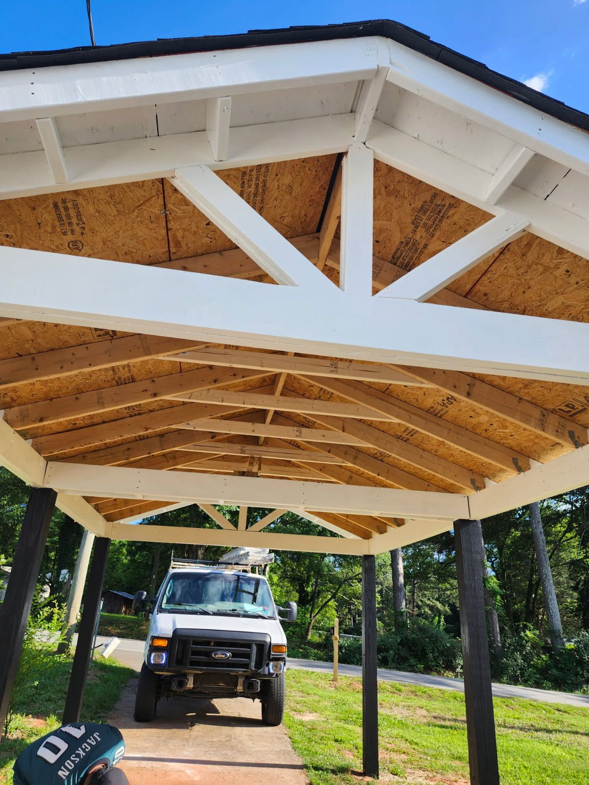 White-framed gazebo with brown underlay, black pillars, and a white van parked underneath on a sunny day.