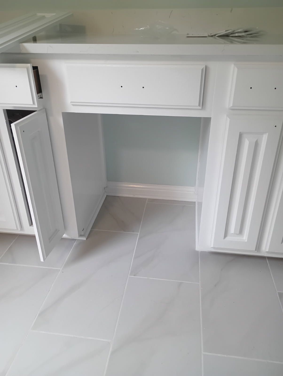 White kitchen cabinets with an open space, gray floor tiles.