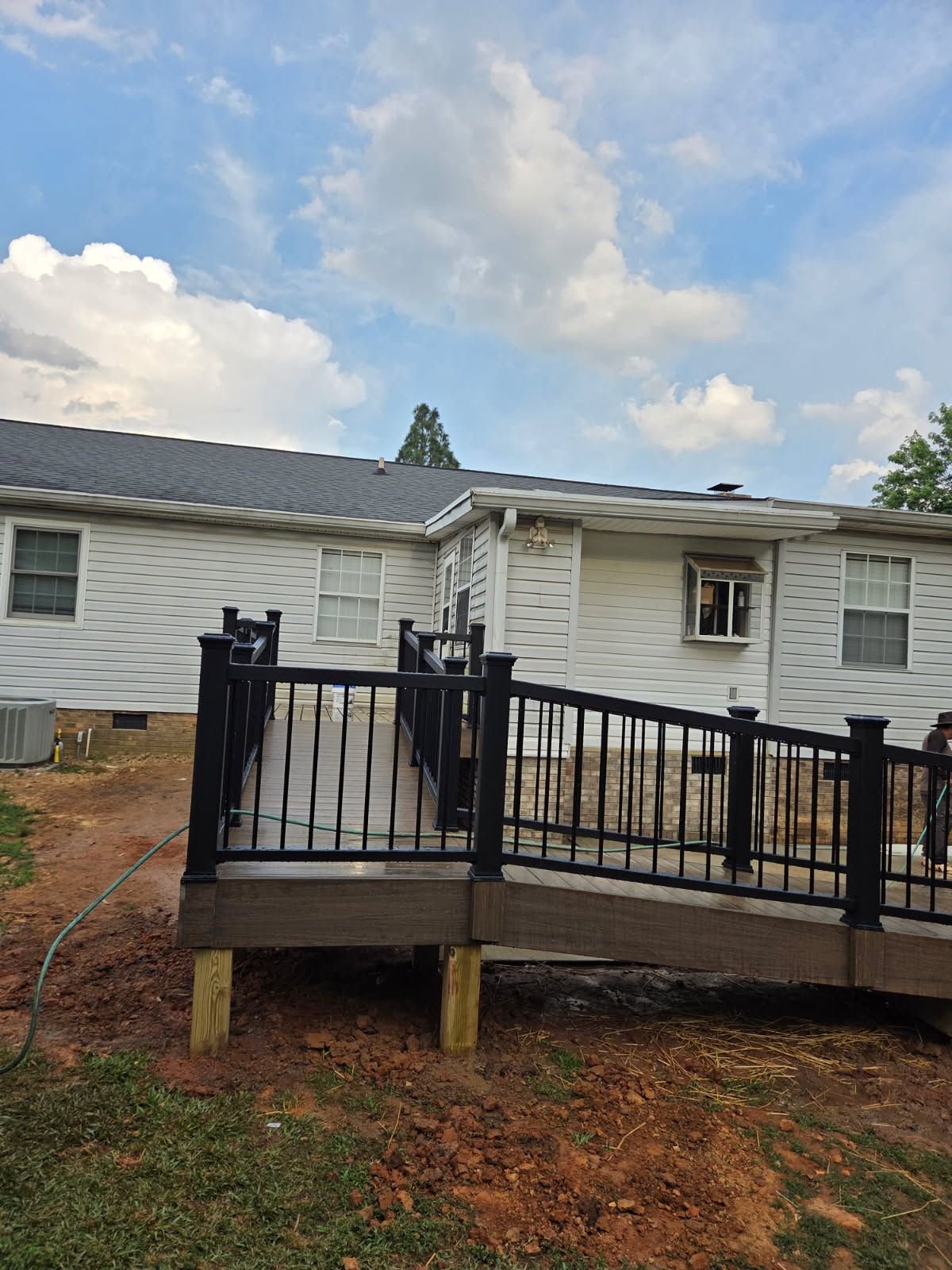 A deck with a ramp attached to a house with gray siding under a cloudy sky.