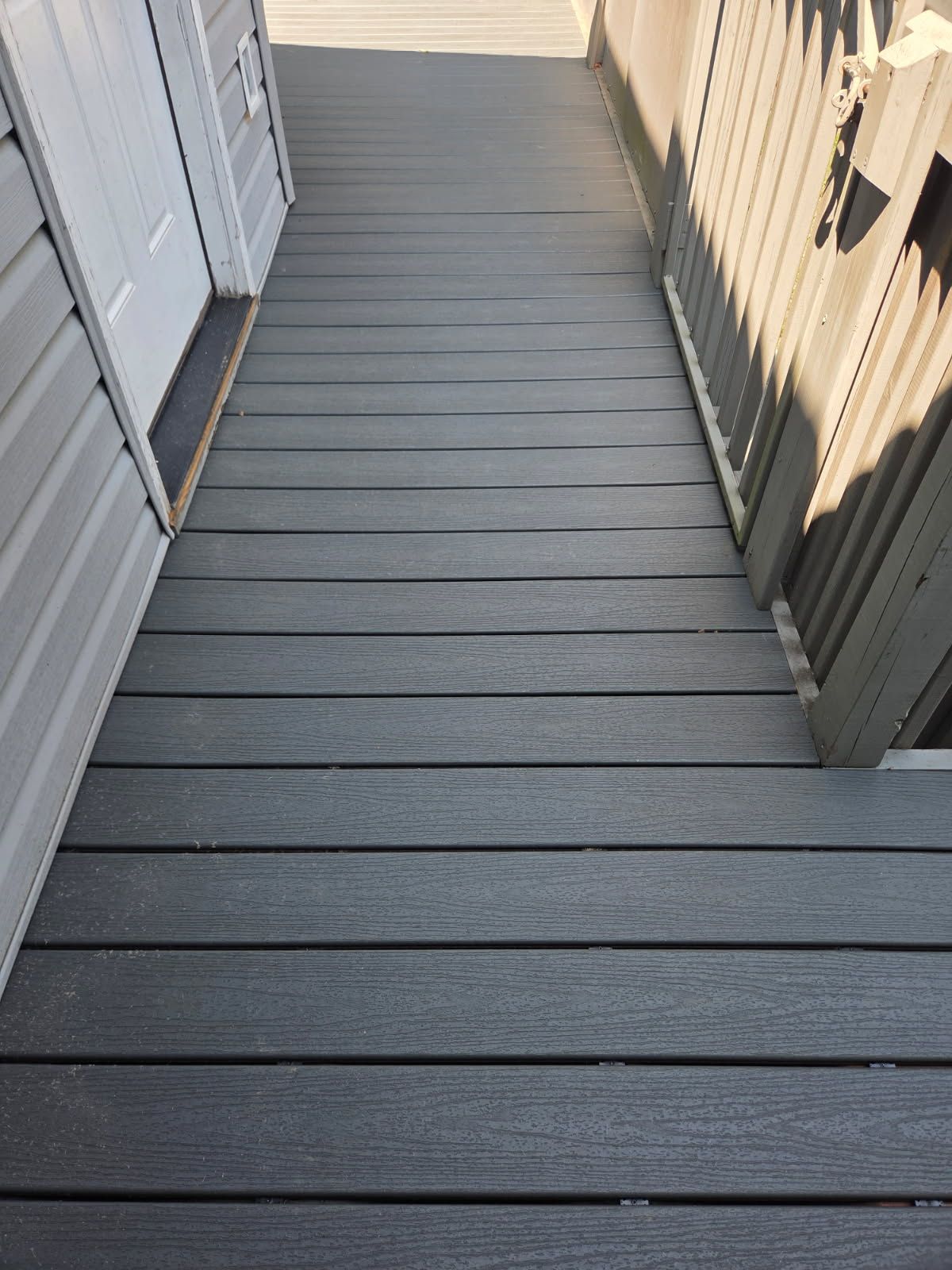 Gray composite deck walkway with a door on the left and a railing on the right.