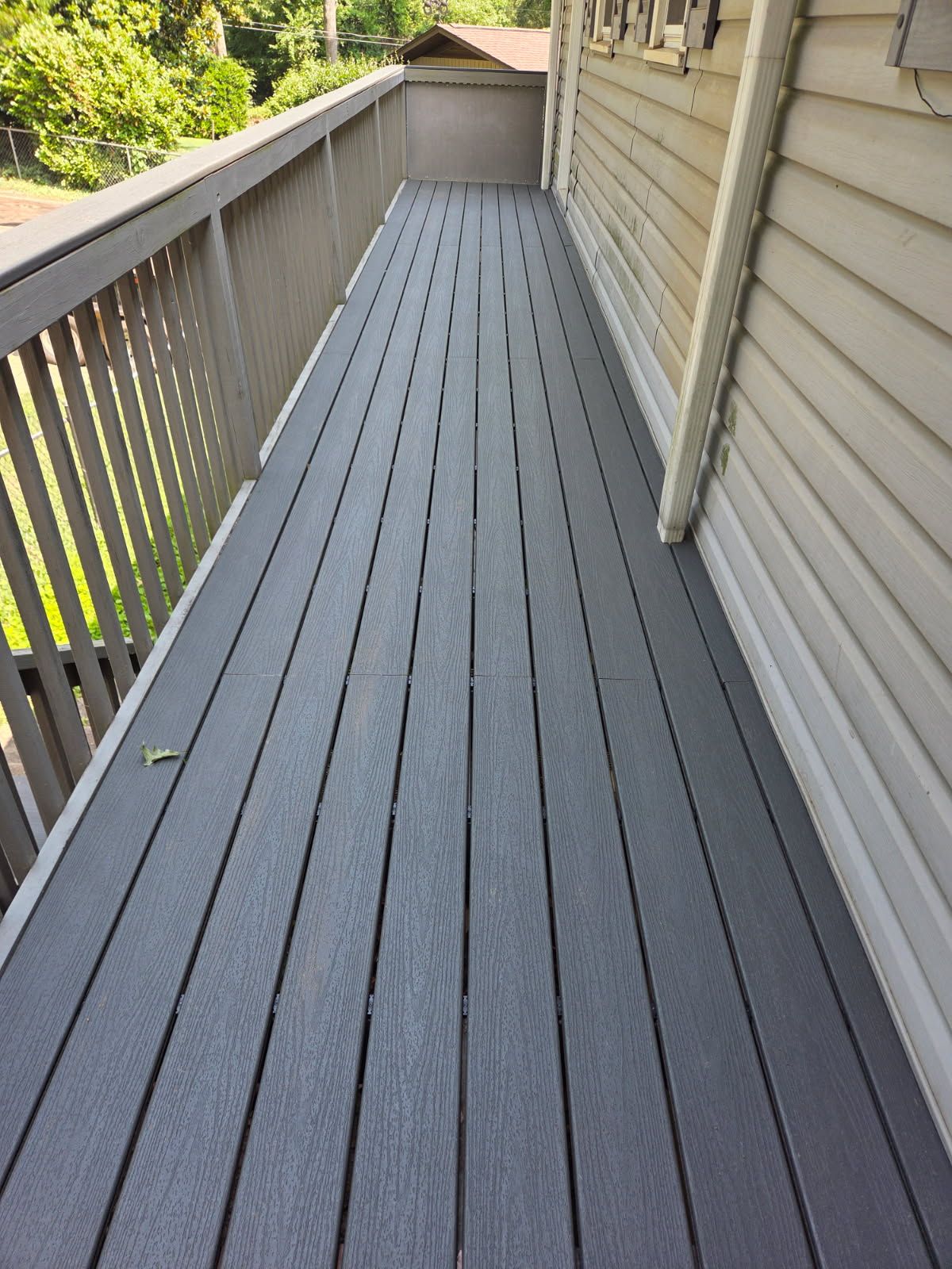 Gray composite deck with railings next to a light-colored house.