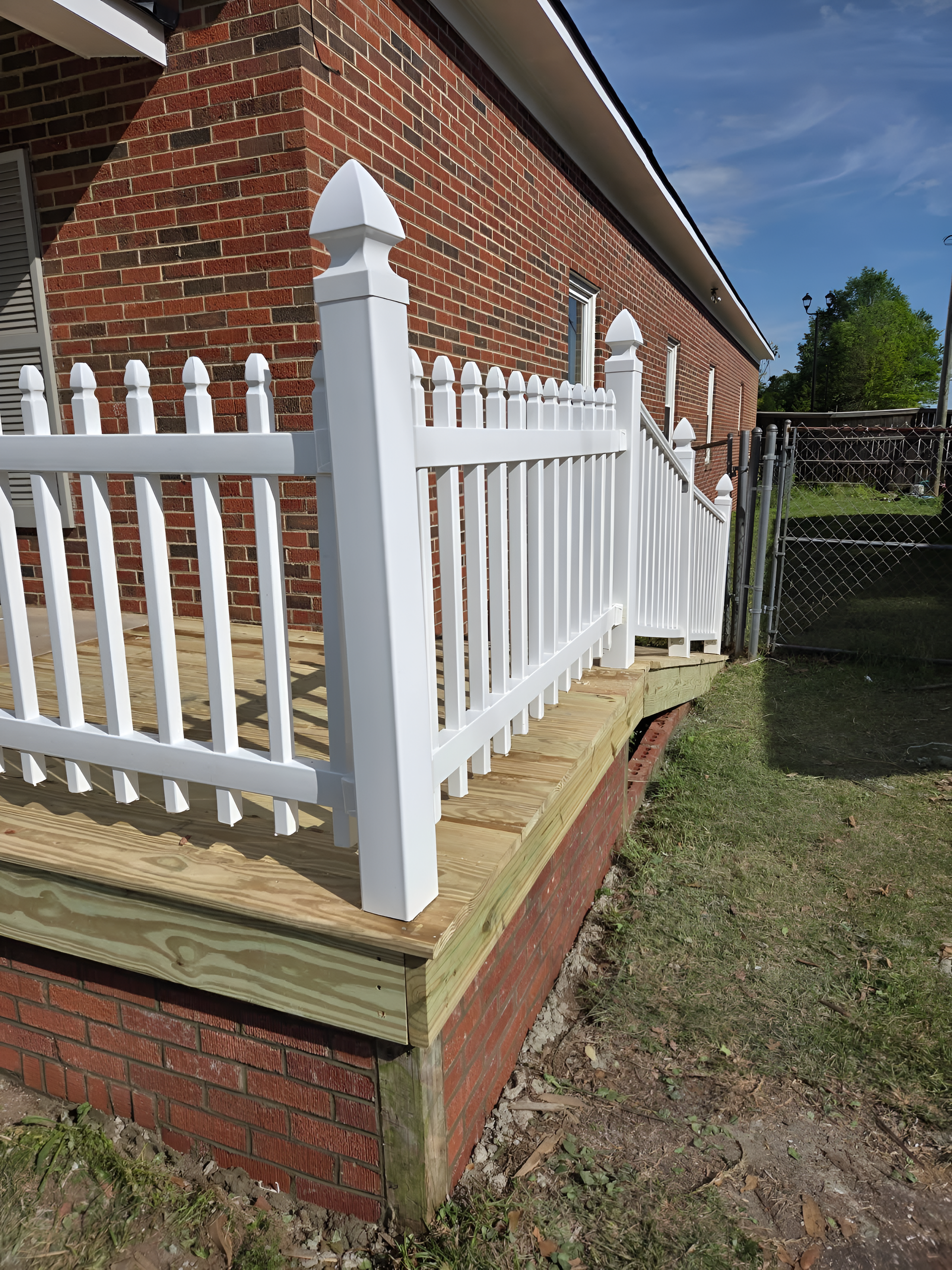 White picket fence on a raised wooden deck with brick exterior.
