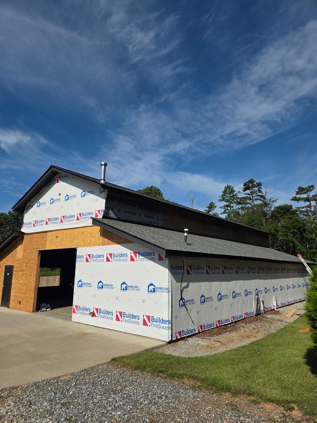 Barn under construction, wrapped in white building wrap; blue sky above.