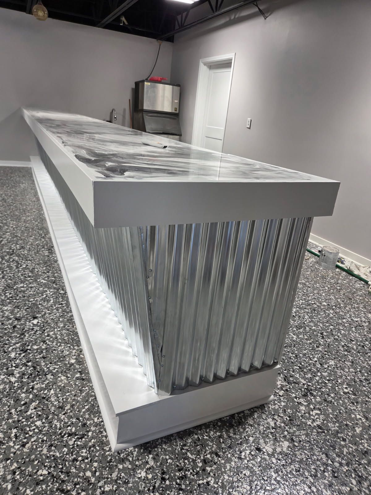 Bar with corrugated metal facade and patterned countertop in a room with a speckled floor.