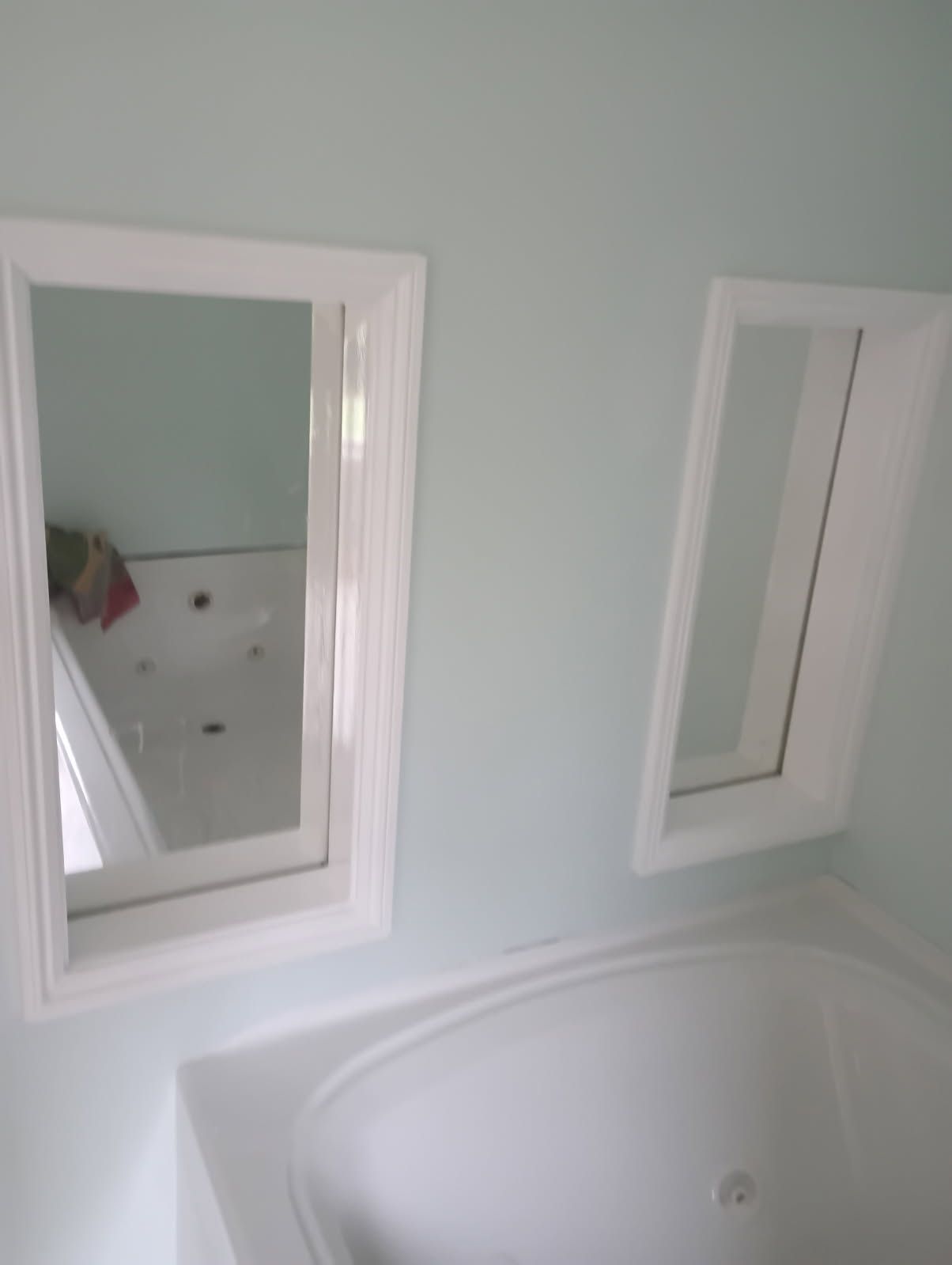 Two recessed mirrors in white frames above a white bathtub, set in a light blue bathroom.