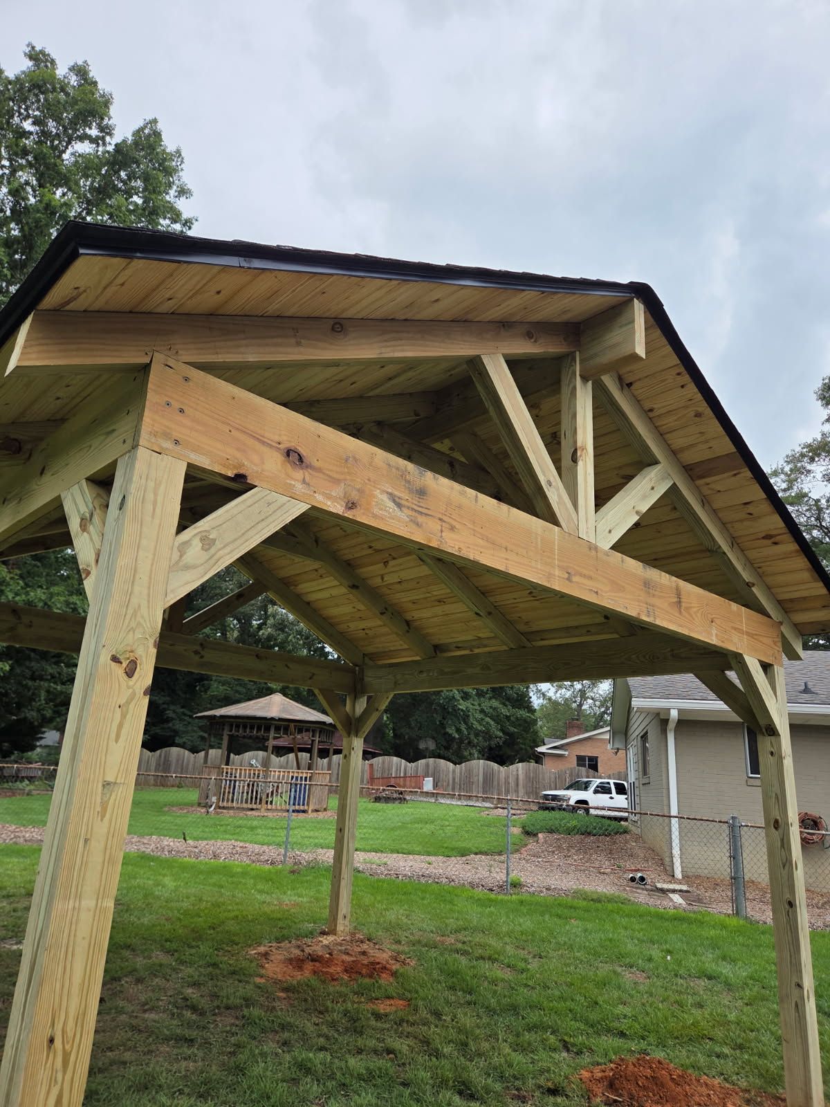 Wooden gazebo under construction in a grassy backyard, with a visible frame, roof, and supports.