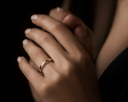 Mani intrecciate, una con un anello d'oro al dito, su uno sfondo scuro.