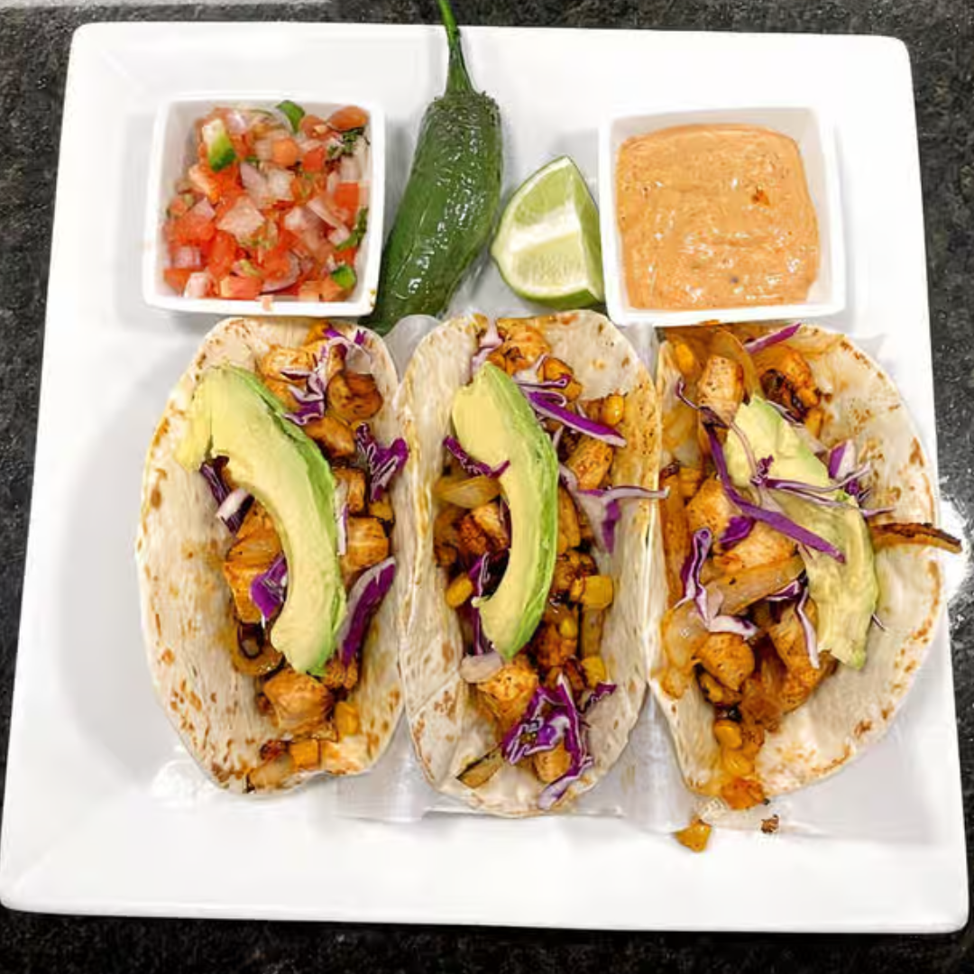 Three tacos with avocado , cabbage , and sauce on a white plate.