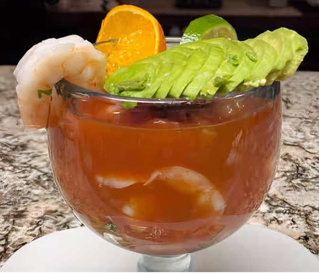 A glass of shrimp , avocado , and orange slices on a table.