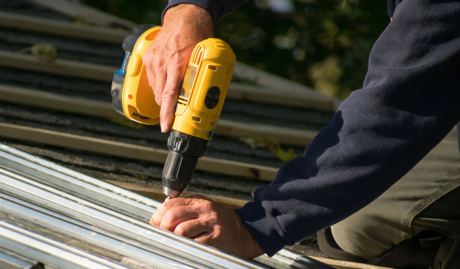 A Man is Working on a Roof With a Drill — Stormguard Roofing In Caloundra West, QLD