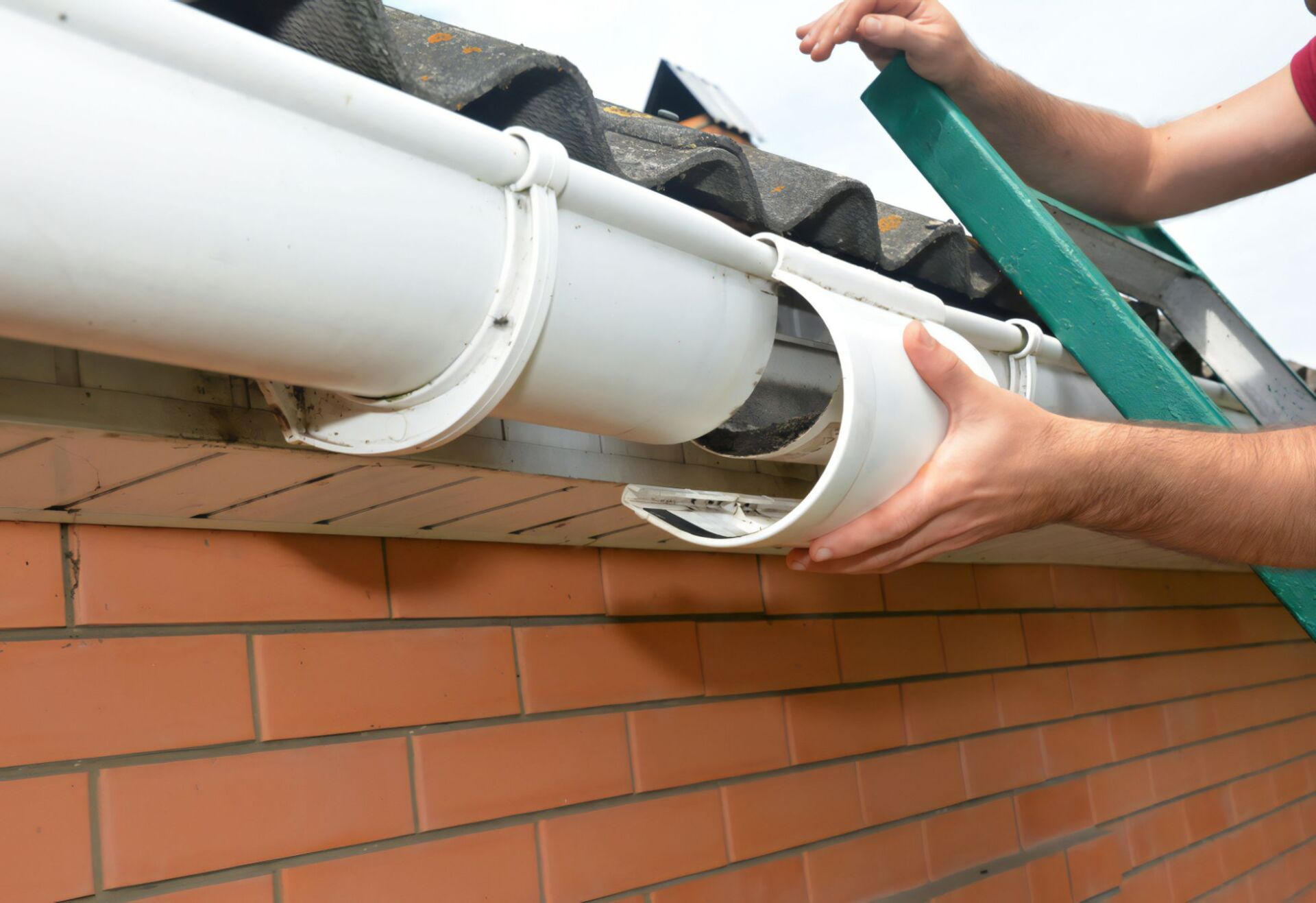 A Man is Installing a Gutter on the Side of a Brick Building — Stormguard Roofing In Caloundra West, QLD