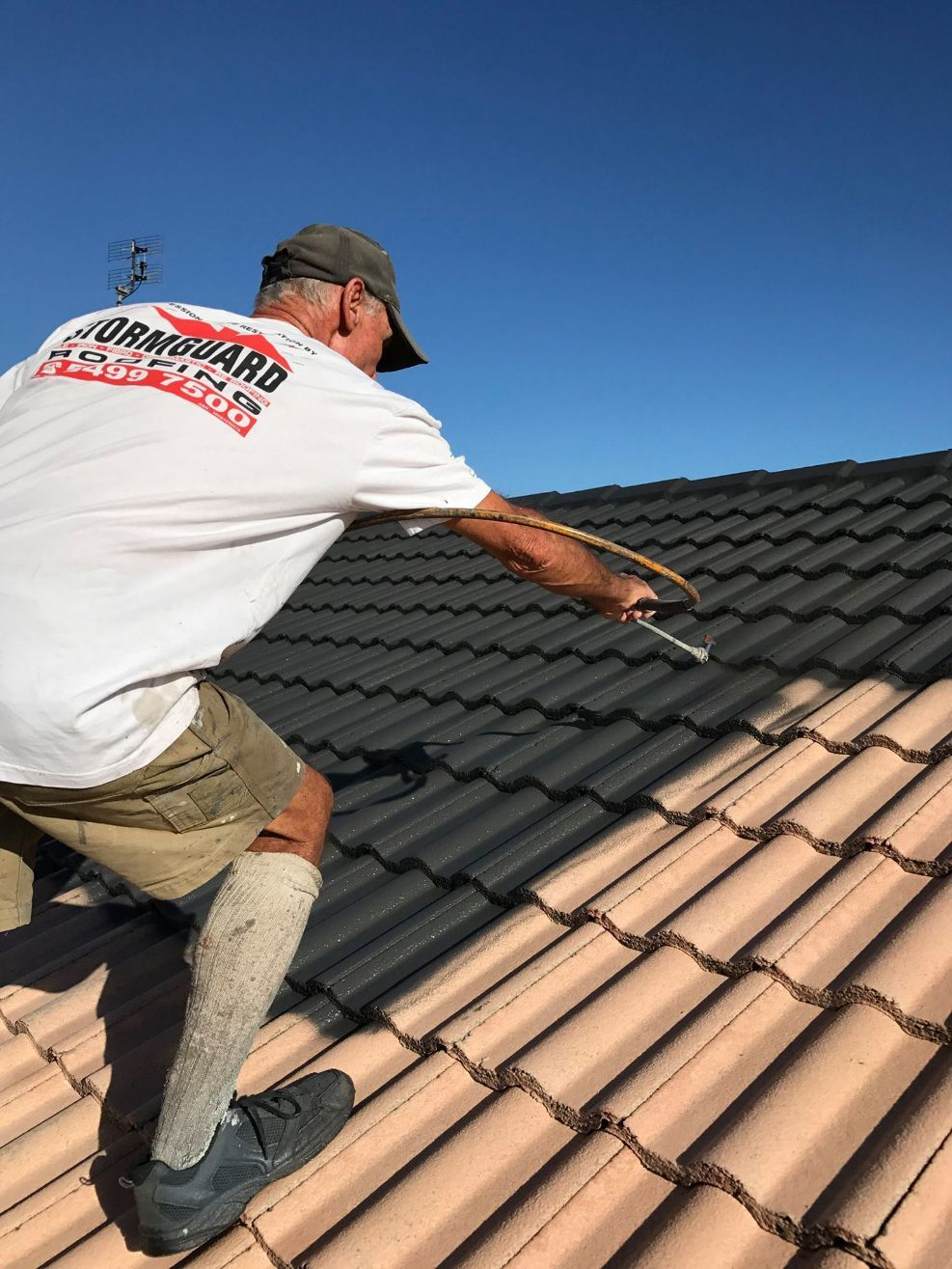 A Man is Painting a Tiled Roof With a Brush — Stormguard Roofing In Caloundra West, QLD