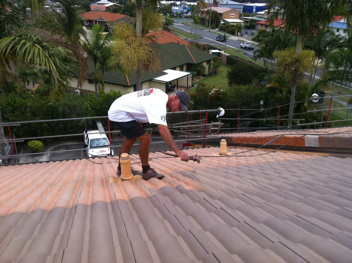 A Man is Working on the Roof of a Building — Stormguard Roofing In Caloundra West, QLD