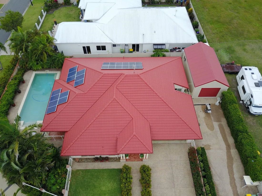 An Aerial View of a House With a Red Roof and Solar Panels on It — Stormguard Roofing In Caloundra West, QLD
