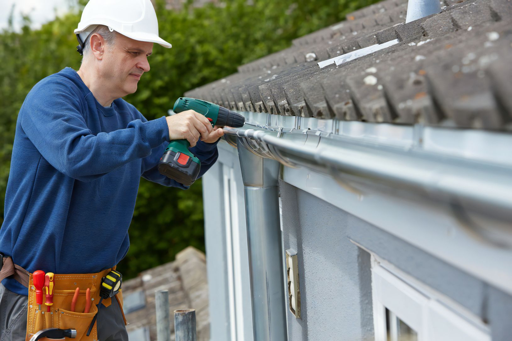 A Man is Installing a Gutter on the Side of a House — Stormguard Roofing In Burpengary, QLD
