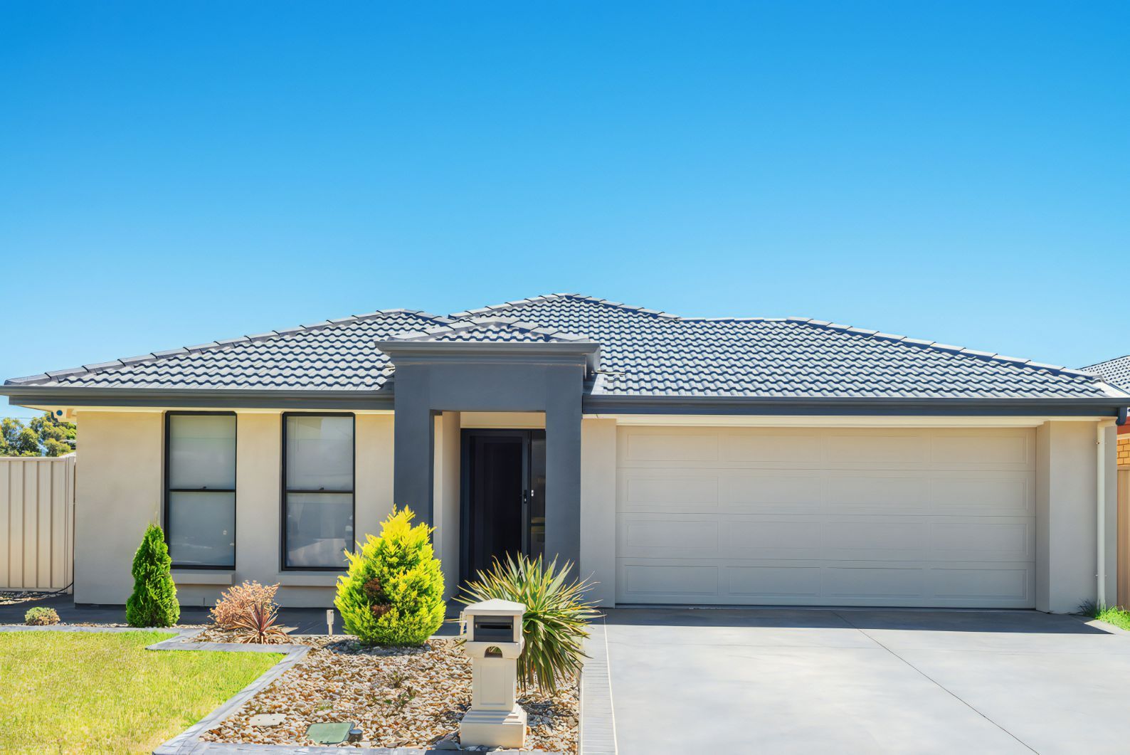 A White House With a Black Roof and a Driveway — Stormguard Roofing In Caloundra West, QLD