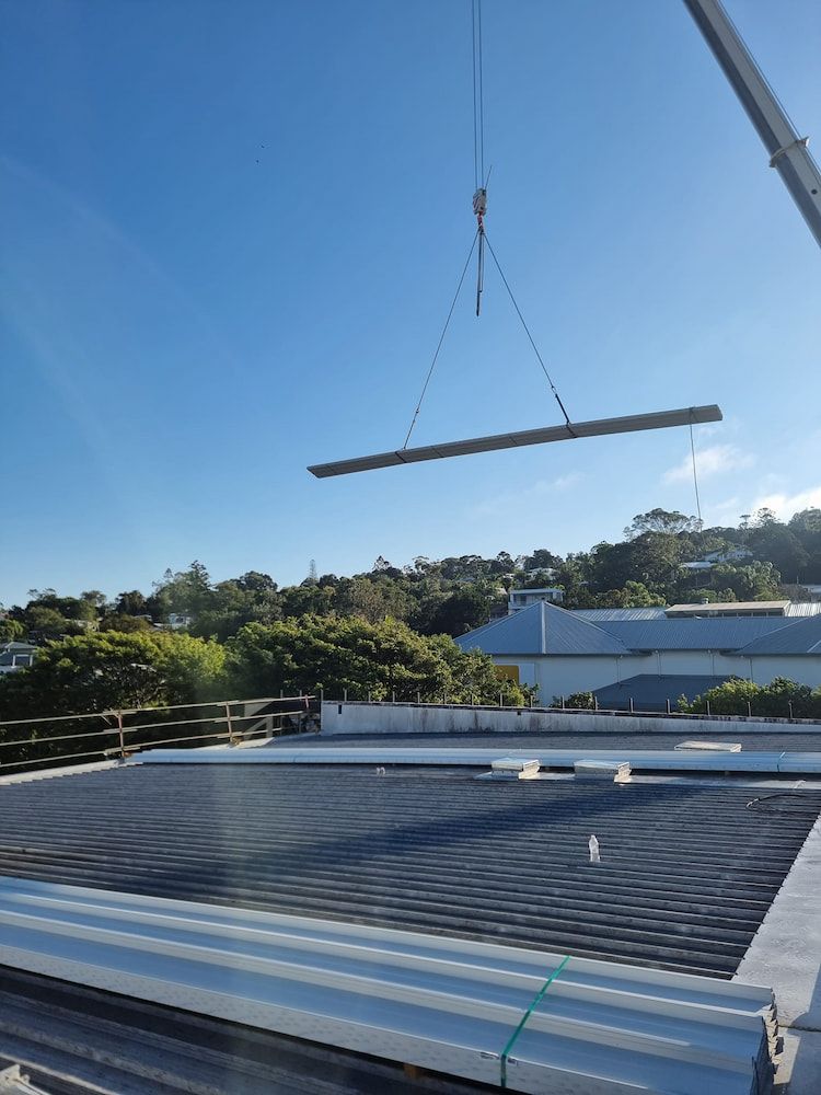 A Crane is Lifting a Piece of Metal on Top of a Roof — Stormguard Roofing In Redcliffe, QLD