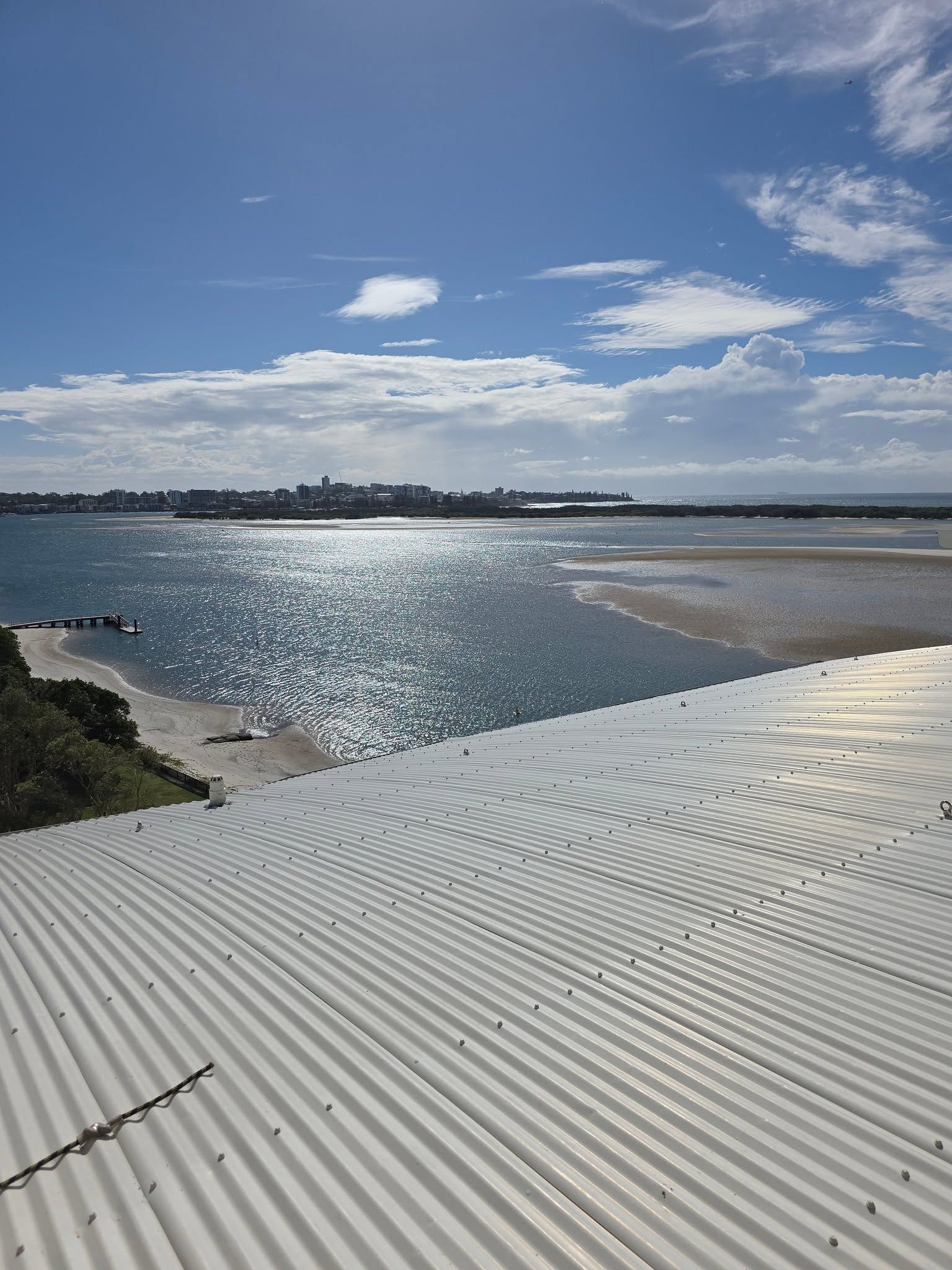 Sunlit Bay With Rippling Water and a Corrugated White Roof in the Foreground — Stormguard Roofing In Caloundra West, QLD