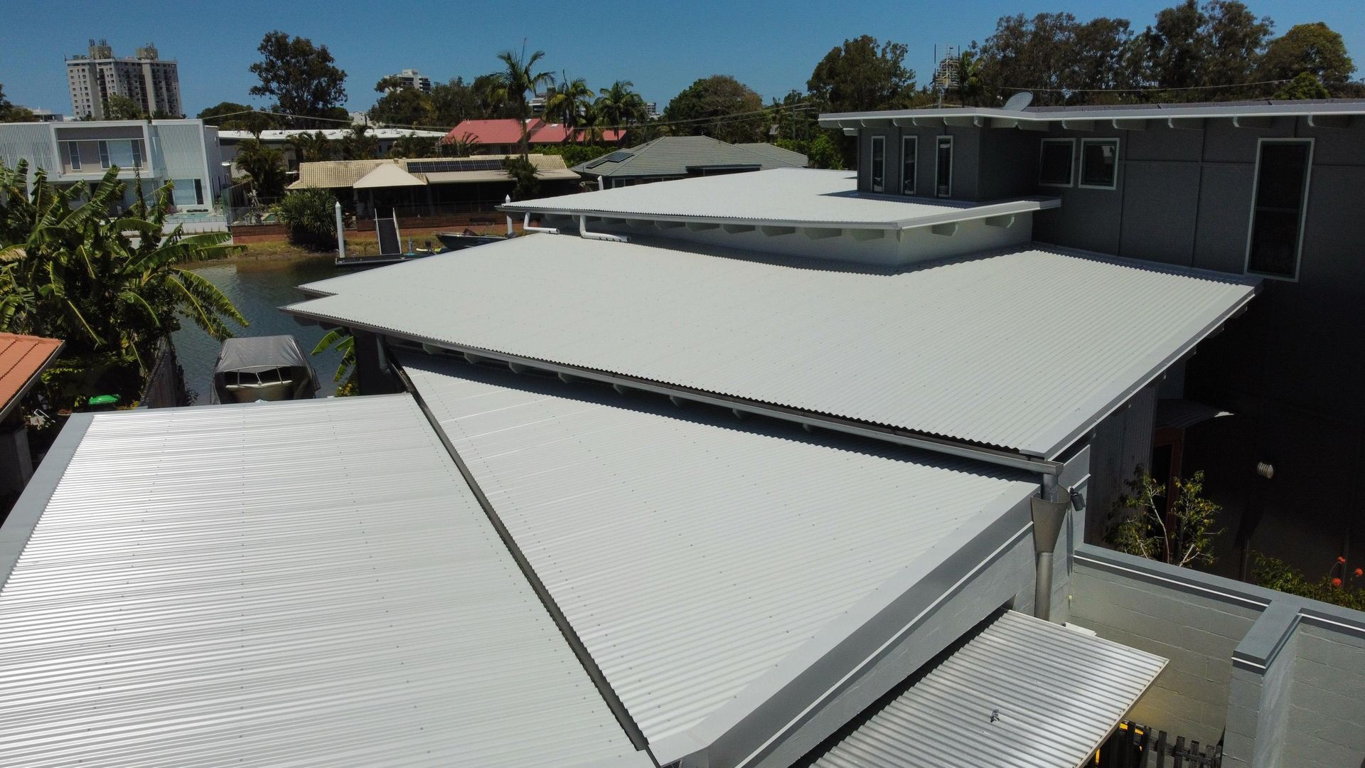 Silver metal roofs on modern homes, trees, and water on a sunny day. — Stormguard Roofing In Caloundra West, QLD
