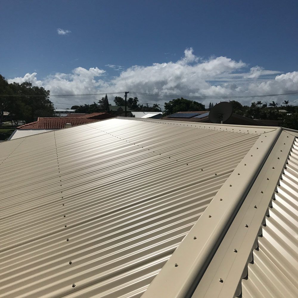 Beige Corrugated Metal Roof Under a Blue Sky With Clouds — Stormguard Roofing In Caloundra West, QLD