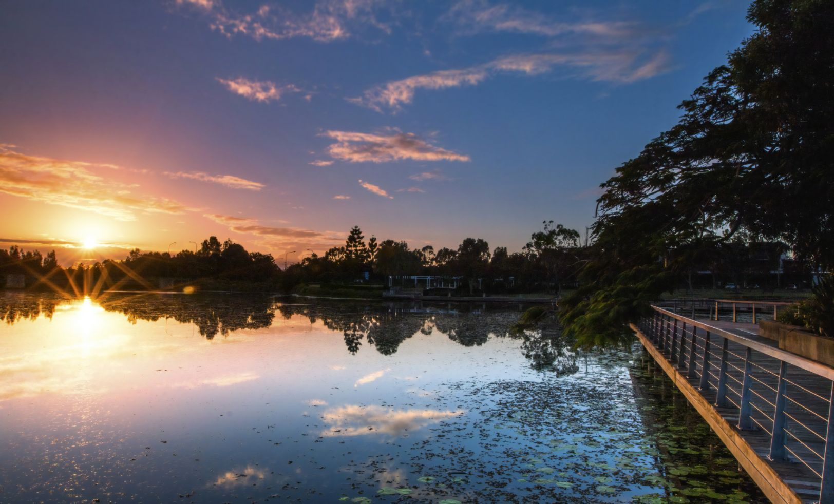 The Sun is Setting Over a Lake With a Bridge in the Foreground — Stormguard Roofing In  North Lakes, QLD