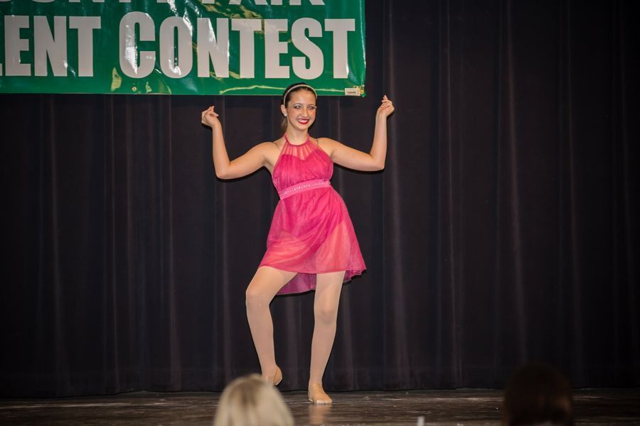 Dancer in a pink dress posing onstage under a “...ENT CONTEST” banner