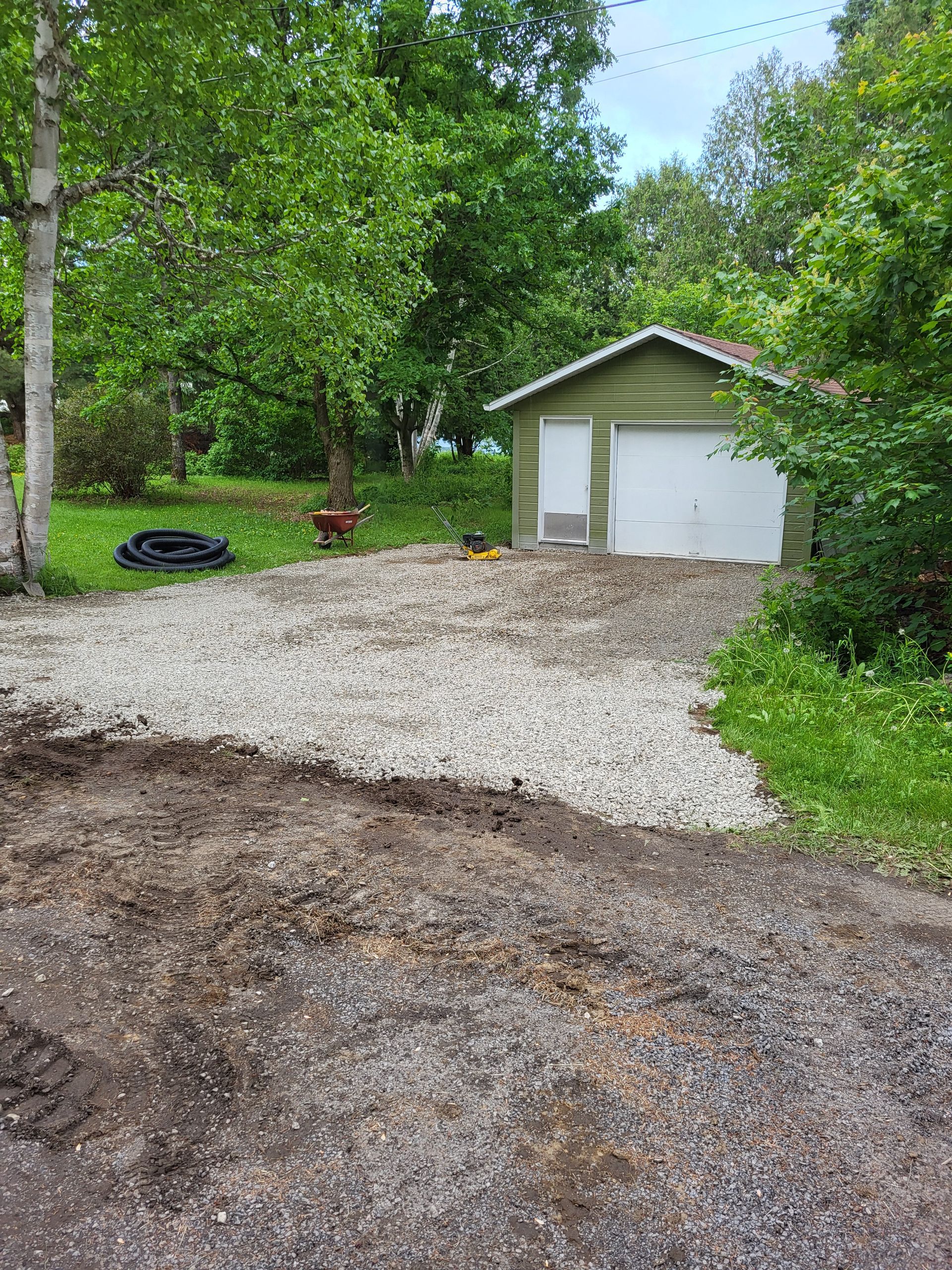 Une allée de gravier avec un garage en arrière-plan et des arbres en arrière-plan.