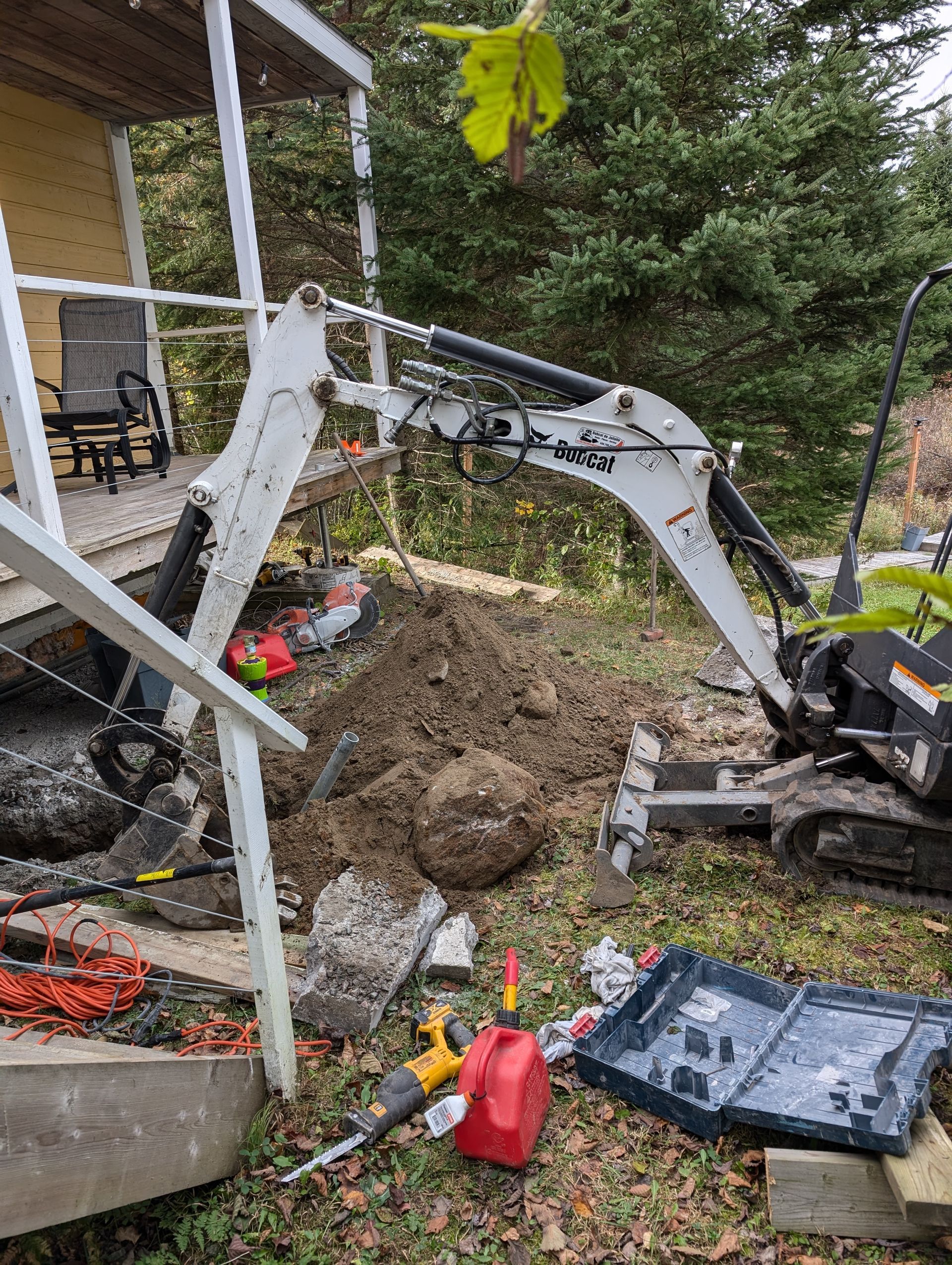 Une petite excavatrice creuse un trou dans le sol devant une maison.