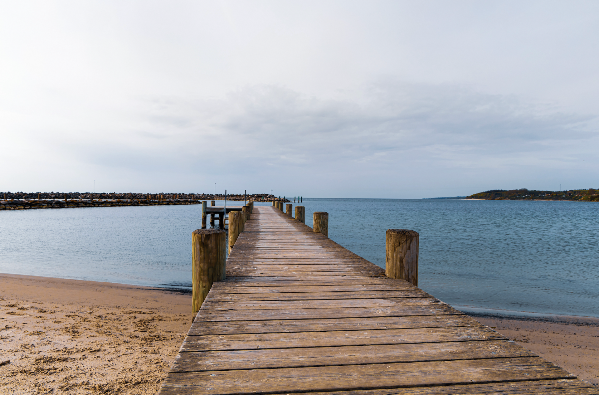 A wooden pier leading into the ocean on a cloudy day.