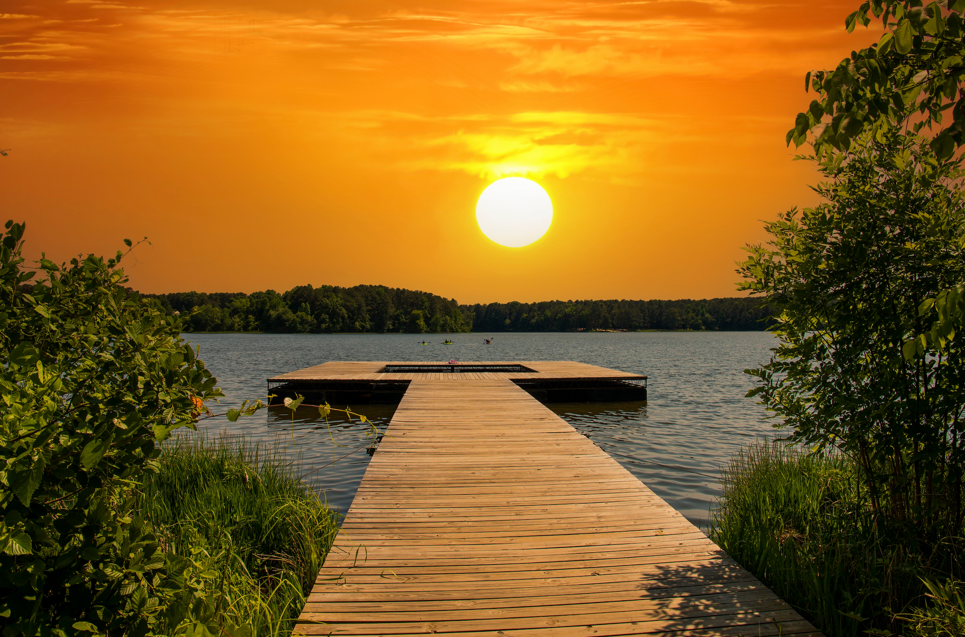 A wooden dock leading to a lake at sunset.