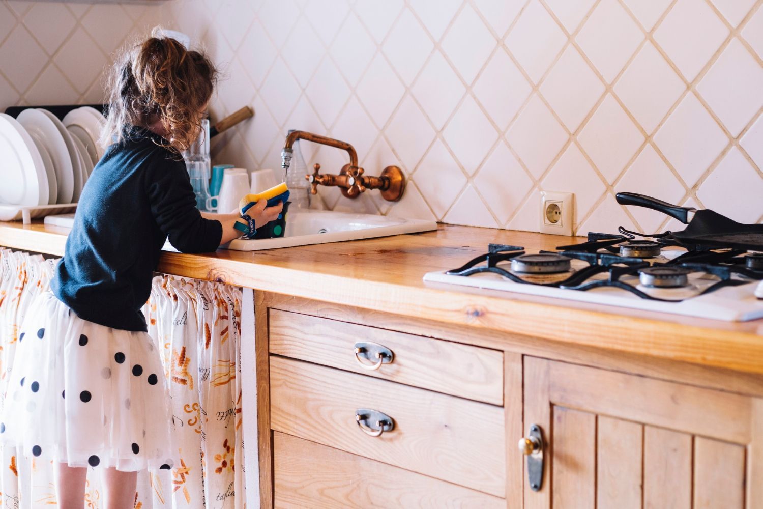 A little girl is cleaning a kitchen counter with a sponge.
