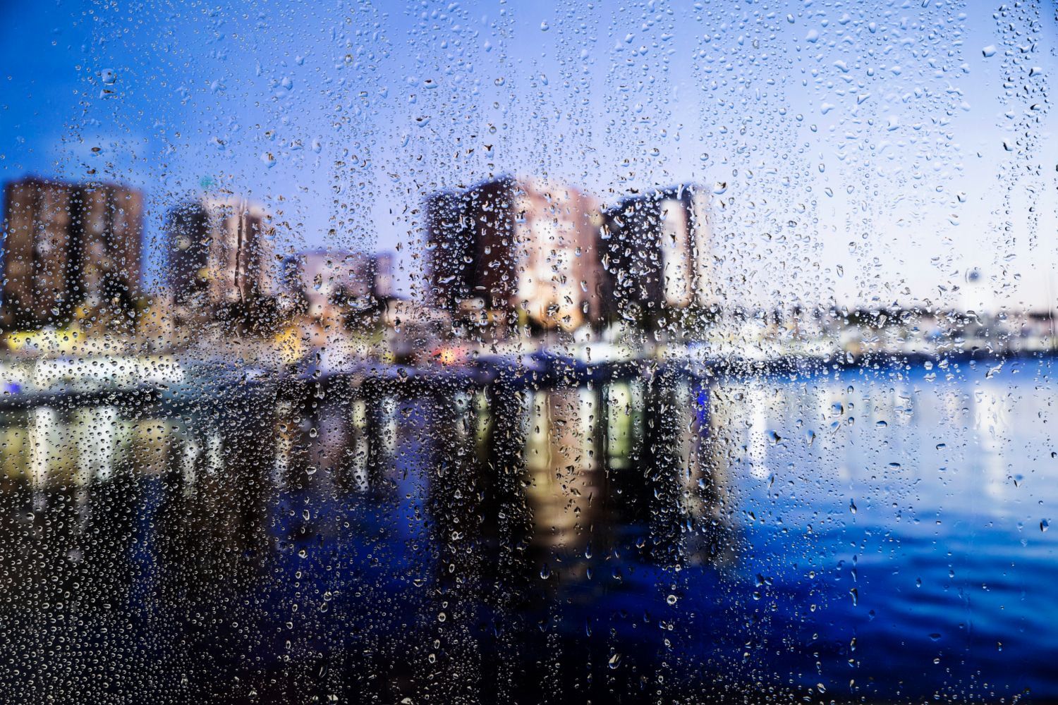 A city skyline is reflected in a window with rain drops on it.