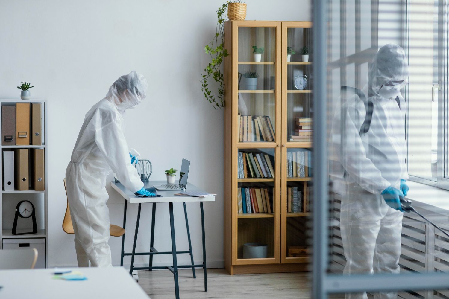 A man in a protective suit is cleaning a desk in an office.