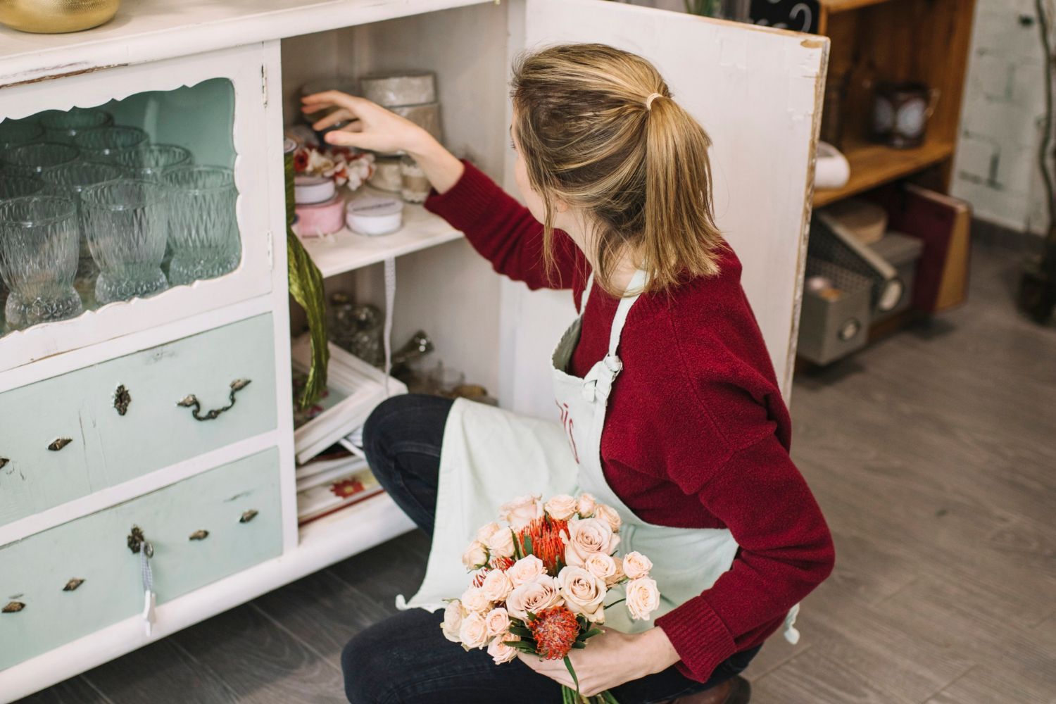 A woman is kneeling down in front of a cabinet holding a bouquet of flowers.