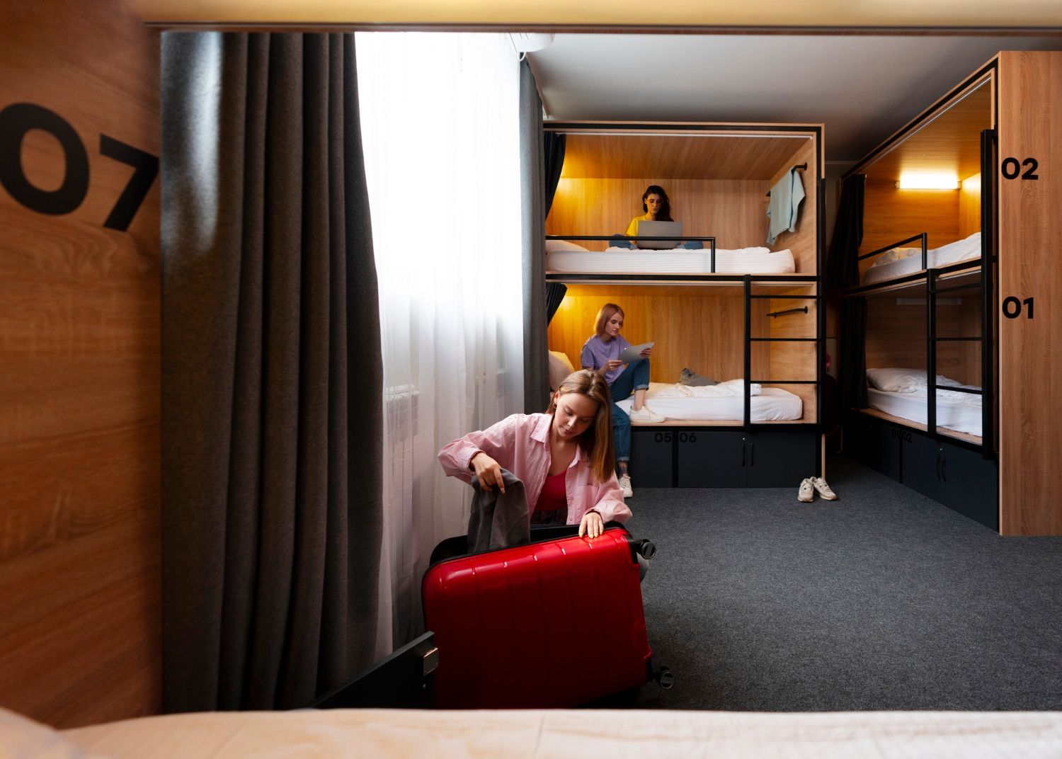 A woman is sitting on a bed with a suitcase in a room with bunk beds.